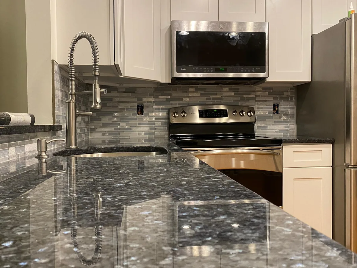 A kitchen with dark speckled granite counters, a gray tiled backsplash, and stainless steel appliances.