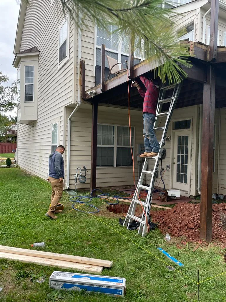 Two workers, one on a ladder, replacing siding and trim on the upper story of a house.