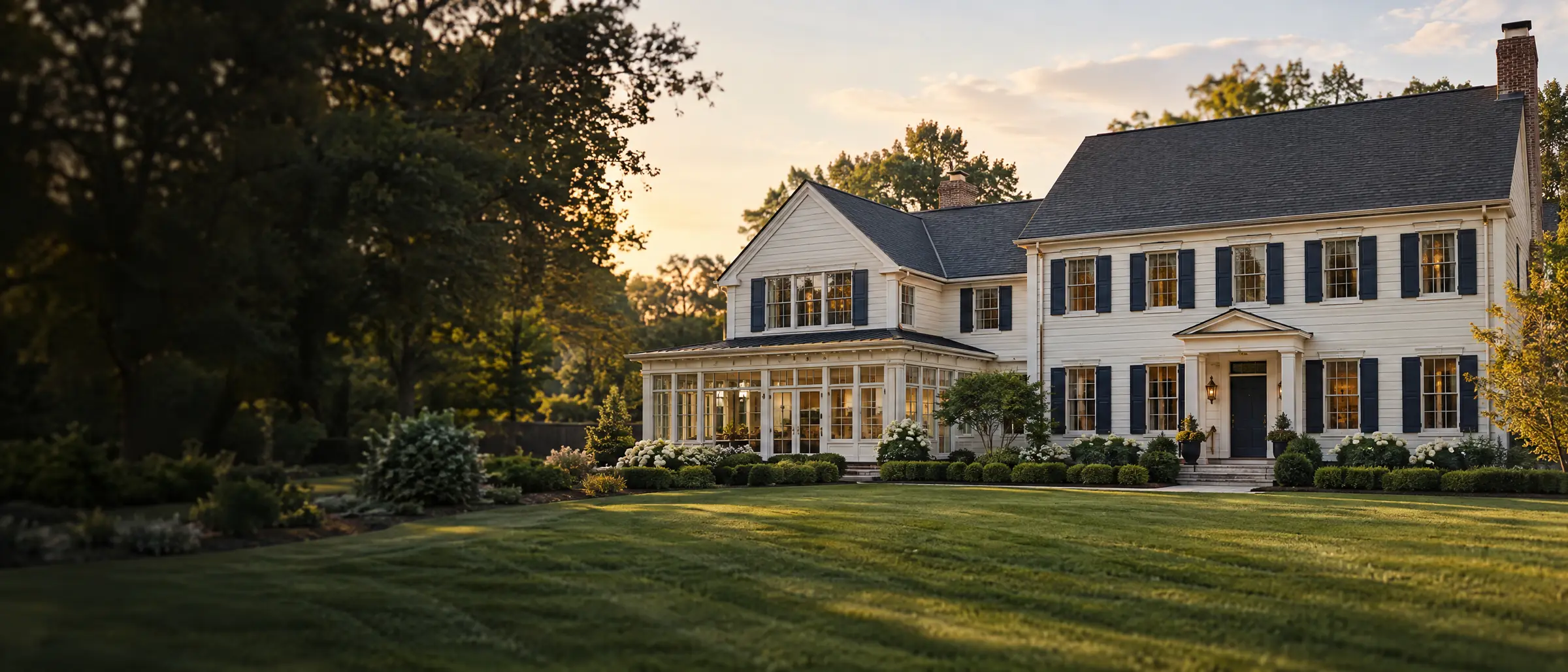 A colonial home with a matching two-story addition and a sunroom, at golden hour